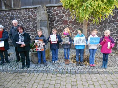 Schulkinder zeigen vor der Erinnerungsstele ihre selbst gestalteten Mahnbilder